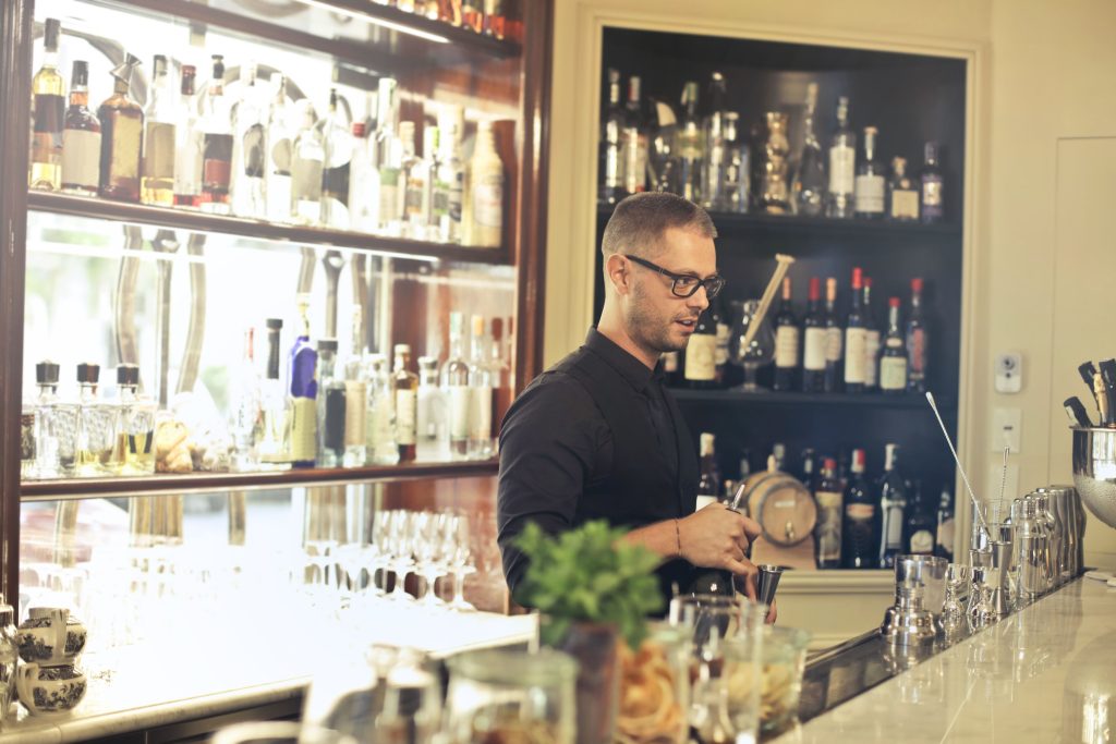 Bartender preparing cocktails behind a bar counter, illustrating the best POS system for bars