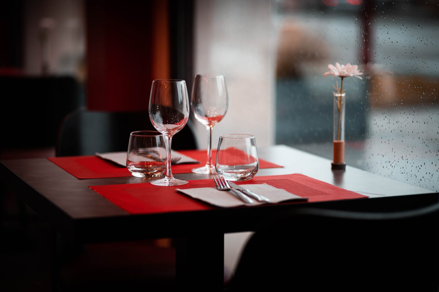 Restaurant marketing detail: a set table by a rain-streaked window before service