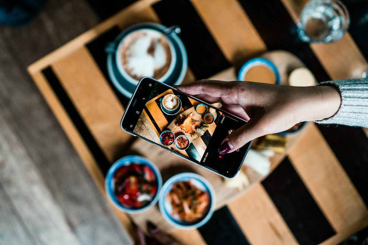 AI for restaurant marketing: a guest photographs coffee and pastries on a phone at a cafe table