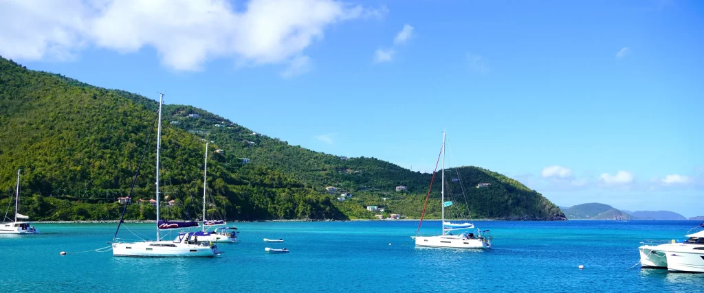 Sailboats at anchor in Cane Garden Bay, Tortola, with green hills rising behind the beach.