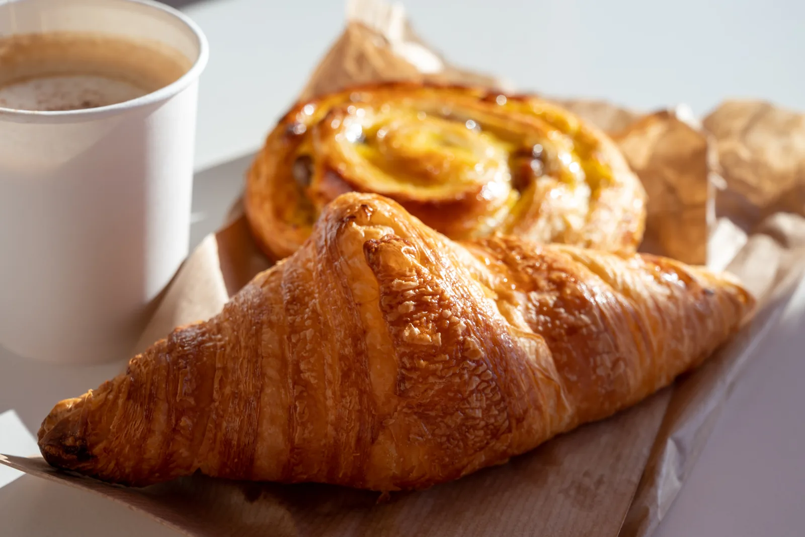 Fresh-baked pastries and a coffee on a paper-lined tray in morning light.