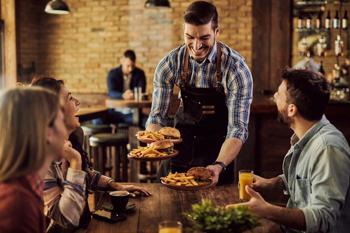 How to increase restaurant revenue: a server bringing plates to a full table of guests
